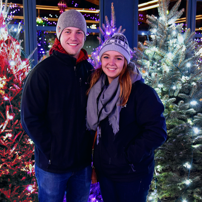 Couple smiling in front of lit trees
