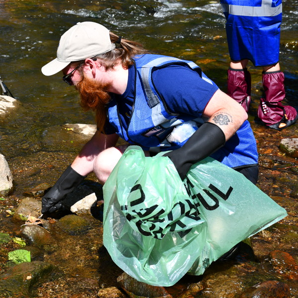 Man in blue vest cleaning up trash from river